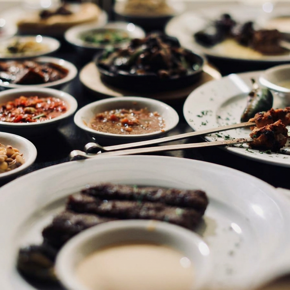 Table filled with Middle Eastern dishes, including grilled skewers, kebabs, dips, salads, and small bowls of sides.